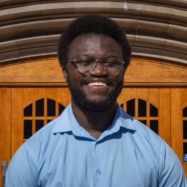 Headshot of Jerome Hamilton Jr. in a light blue polo, standing in front of wooden double doors.