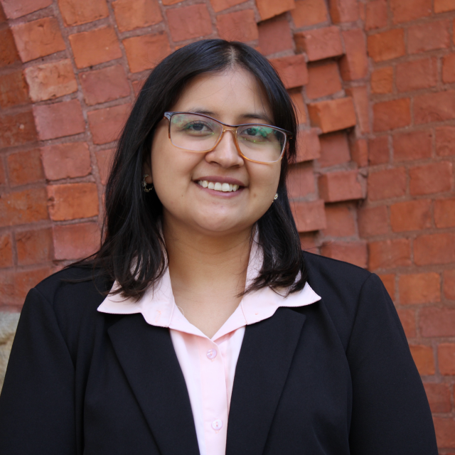 Headshot of Abigail Rodriguez in a light pink collared shirt and black blazer. The background is a red brick wall.