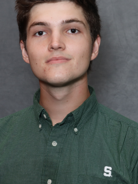 Caden Wade is wearing a green Spartan button down and is standing against a gray background.