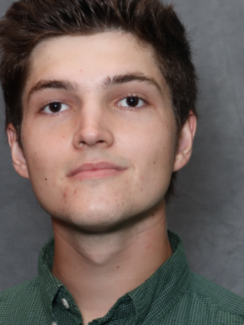 Caden Wade is wearing a green Spartan button down and is standing against a gray background.