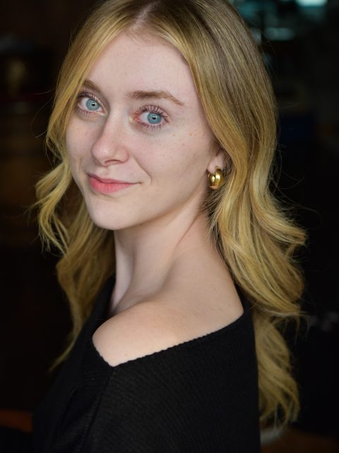 Grace Showerman is wearing a black shirt and smiling at the camera