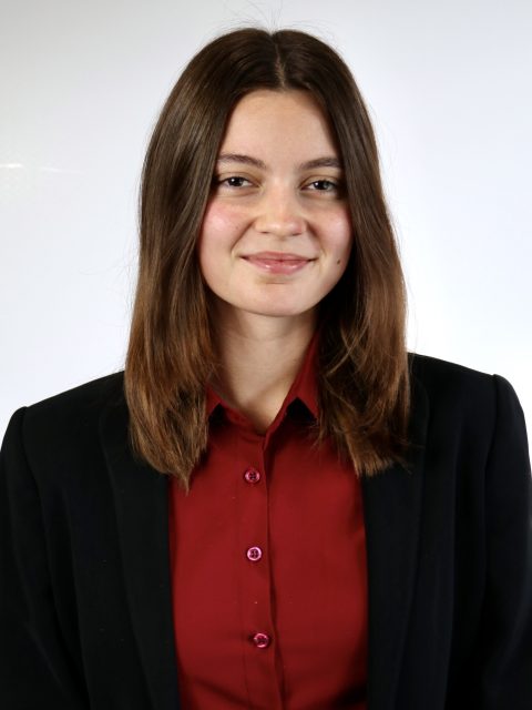 Samantha Schulte is wearing a black blazer and red button down, smiling at the camera.