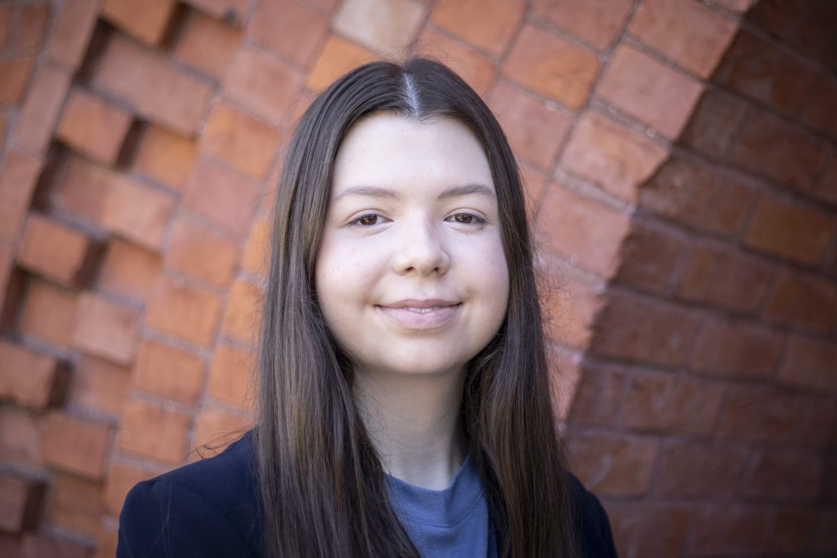 Eleanor Pugh smiles at the camera, wearing a black blazer and standing in front of a brick wall.