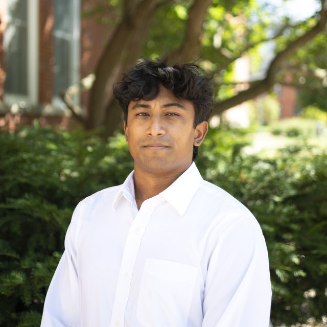 Image of Michigan State University alum Andre Edmond in a white collared shirt, with greenery and a red brick building in the background.