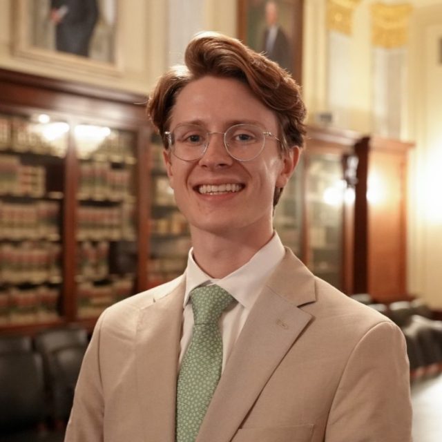 Image of Michigan State University alum Truman Forbes smiling in a tan suit jacket, white collared shirt, and green necktie.