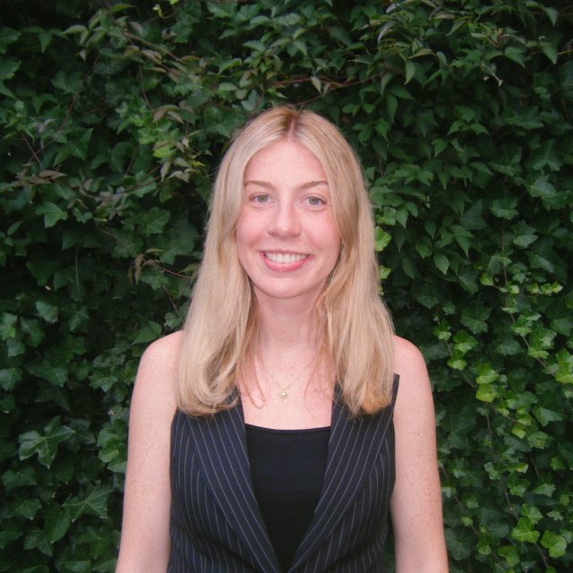 Image of Michigan State University student Ashlin Stover smiling in a striped black vest and black top, with greenery in the background.