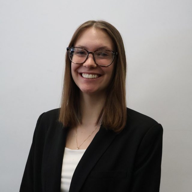 Grace Gramza is smiling at the camera, wearing a black blazer and glasses.