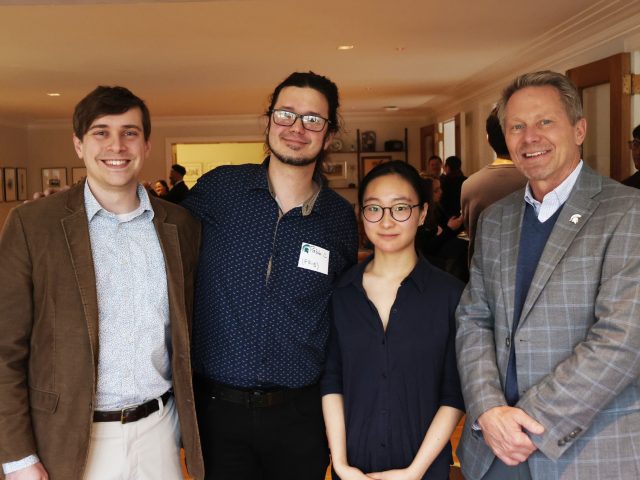 Image of Michigan State University faculty member Kyle Godbey, Honors College student Lauren Jin, faculty member Pablo Giuliani, and President Kevin Guskiewicz standing together and smiling at a mentor appreciation event in Cowles House. They are all in business attire.