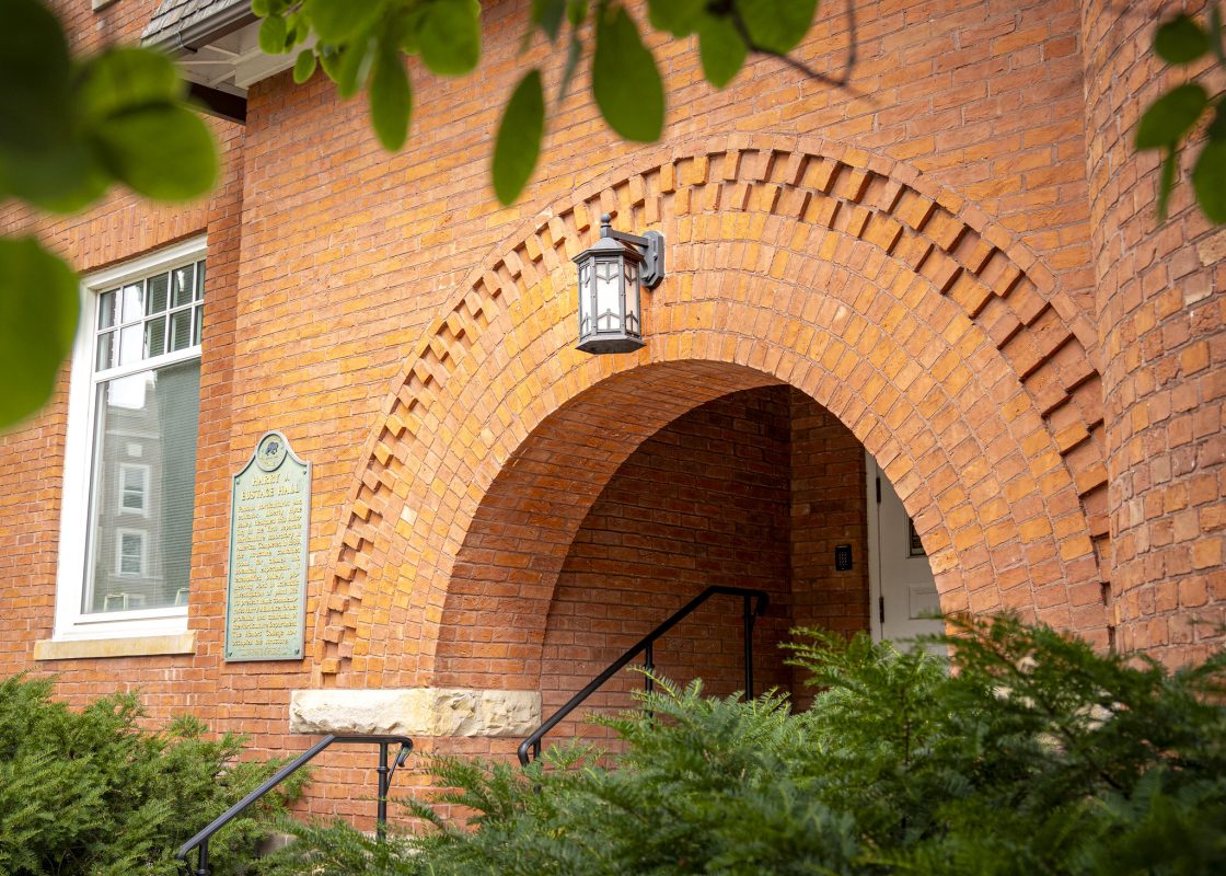 Image of Eustace-Cole Hall on Michigan State University's campus. The red brick building has an arched entrance and is surrounded by lush greenery.