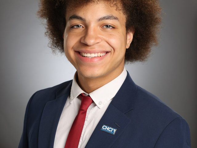 Professional image of Michigan State University student Roberto (Marcos) Garcia smiling in a navy blazer, white collared shirt, and red tie. The background is a gray gradient.