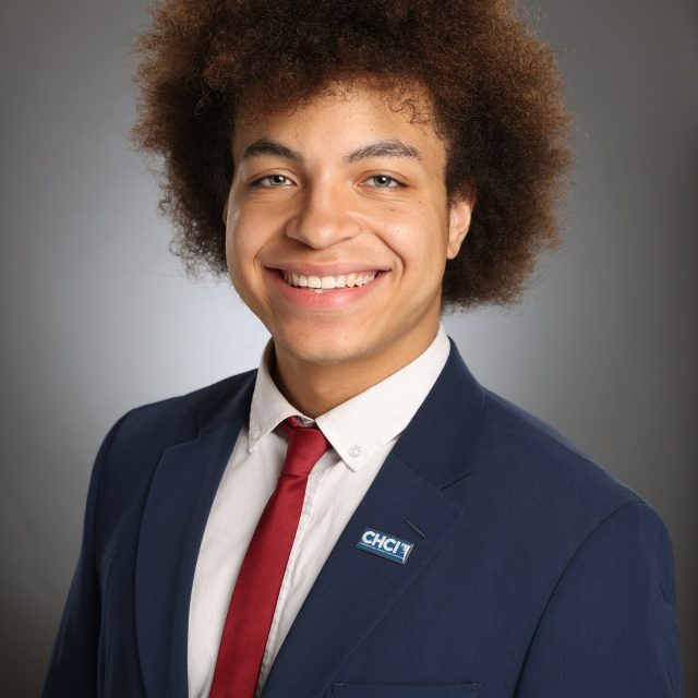 Professional image of Michigan State University student Roberto (Marcos) Garcia smiling in a navy blazer, white collared shirt, and red tie. The background is a gray gradient.