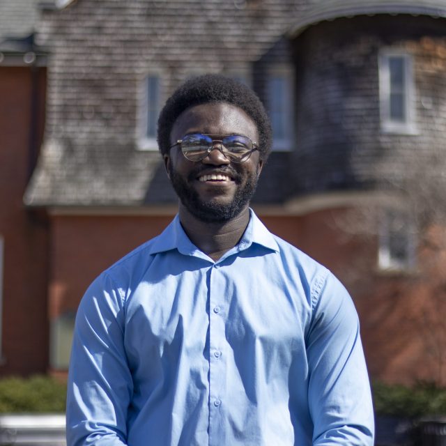 MSU Honors College alumnus and Rhodes Scholarship nominee Jerome Hamilton, wearing a blue button down shirt and standing in front of a red brick facade of Eustace-Cole Hall.